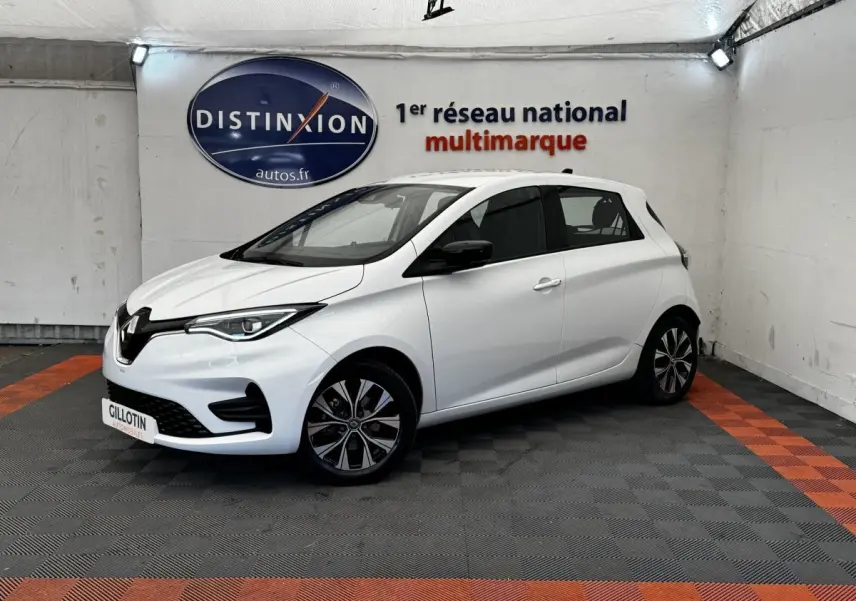 Renault ZOE Iconic R135 blanc vue 3/4 avant droit, avec jantes spécifiques et phares LED allumés.