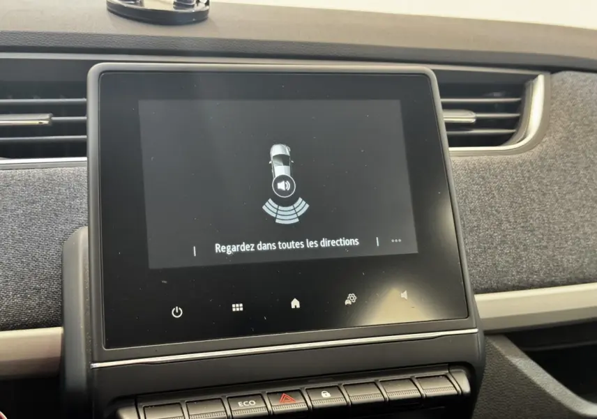 Écran tactile central affichant l'aide au stationnement dans l'habitacle d'une Renault ZOE blanche, vue de face.
