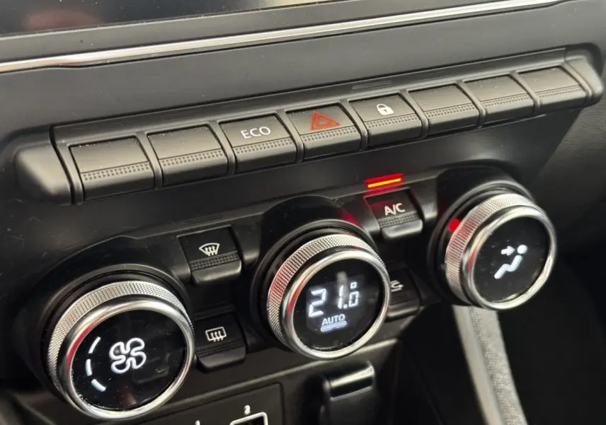 Gros plan sur les commandes de climatisation et boutons multifonctions noirs du tableau de bord de la Renault ZOE blanche.