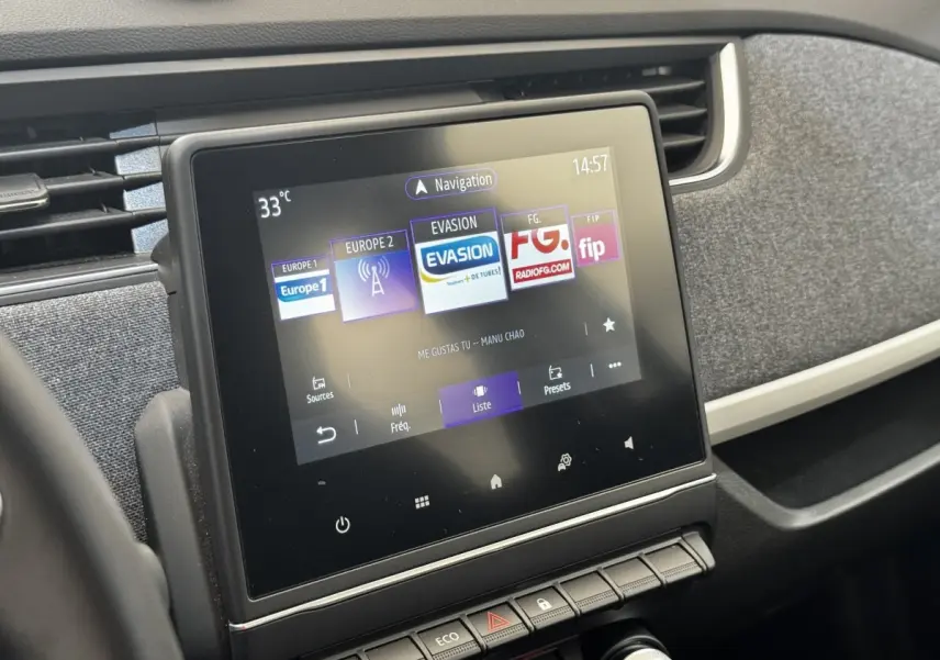 Écran tactile central affichant la radio dans l’habitacle sombre d’une Renault ZOE blanche Iconic R135 vue de face.