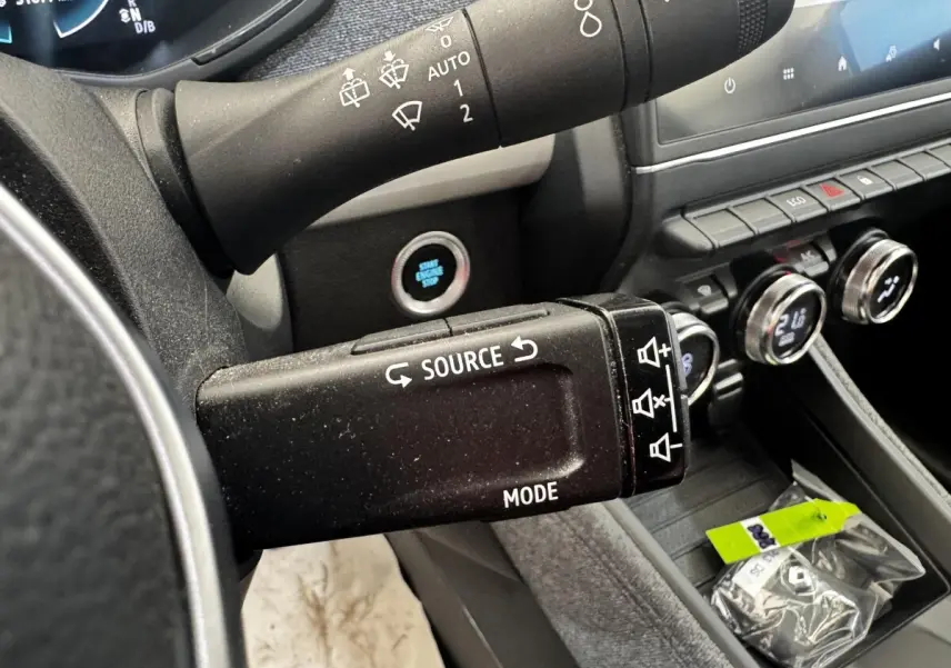 Gros plan sur la commande multimédia au volant d’une Renault ZOE blanche, avec tableau de bord et bouton démarrage visibles.