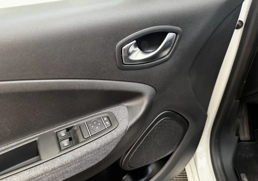 Vue rapprochée de la porte avant gauche blanche d’une Renault ZOE Iconic R135 avec commandes de vitres et poignée intérieure chromée.
