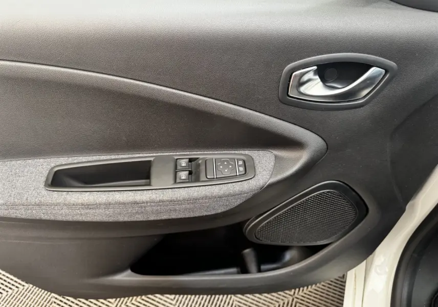 Détail de la porte avant gauche blanche d’une Renault ZOE Iconic R135 avec commandes de vitres et haut-parleur intégré.