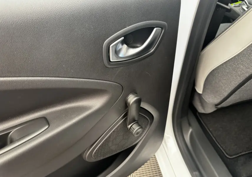 Détail de la porte arrière droite intérieure noire d'une Renault ZOE blanche, avec manivelle de vitre manuelle visible.