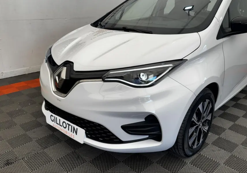Vue 3/4 avant droit d'une Renault ZOE Iconic R135 blanche, avec phares LED et calandre noire brillante.