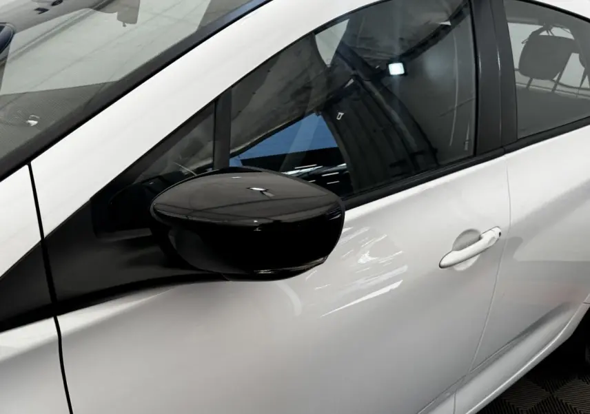 Vue rapprochée du côté gauche d'une Renault ZOE blanche avec rétroviseur noir brillant et poignée de porte blanche.