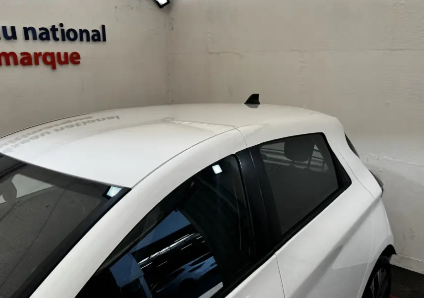 Vue 3/4 arrière droite d'une Renault ZOE Iconic R135 blanche, avec vitres teintées et antenne requin sur le toit.