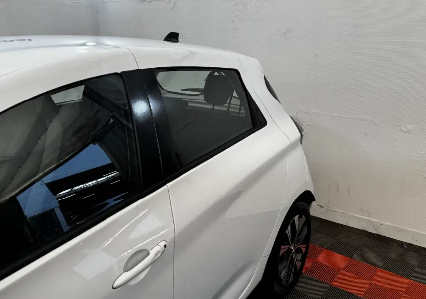 Vue côté gauche arrière d'une Renault ZOE blanche, mettant en valeur la poignée de porte et la jante au design moderne.