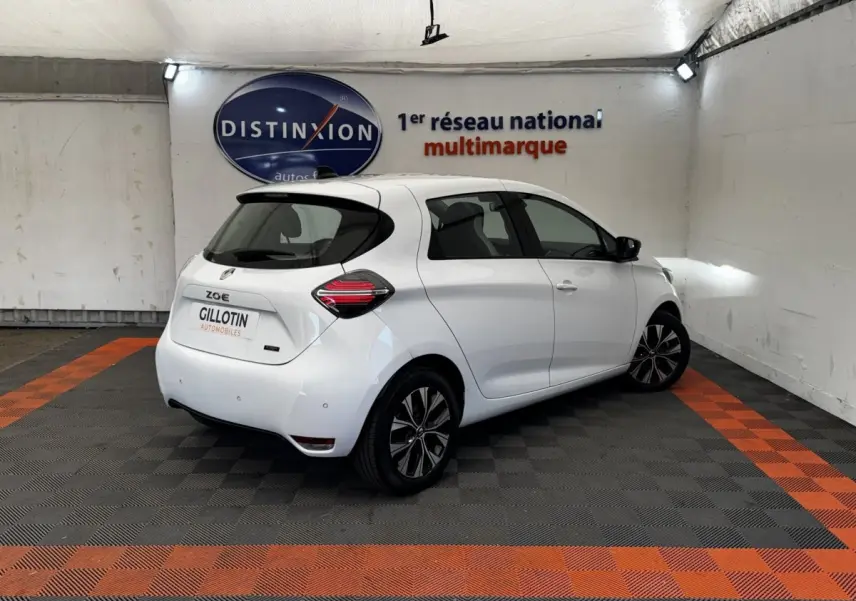 Vue 3/4 arrière droite d'une Renault ZOE blanche électrique avec feux arrière LED et jantes noires stylisées.