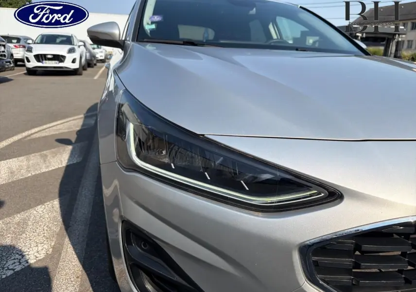 Gros plan sur le phare avant gauche et la calandre chromée d'une Ford Focus gris lunaire métallisé 2023.
