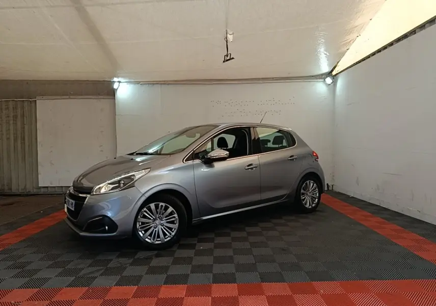 Peugeot 208 Puretech 82 Allure gris clair vue 3/4 avant droit dans un garage éclairé.