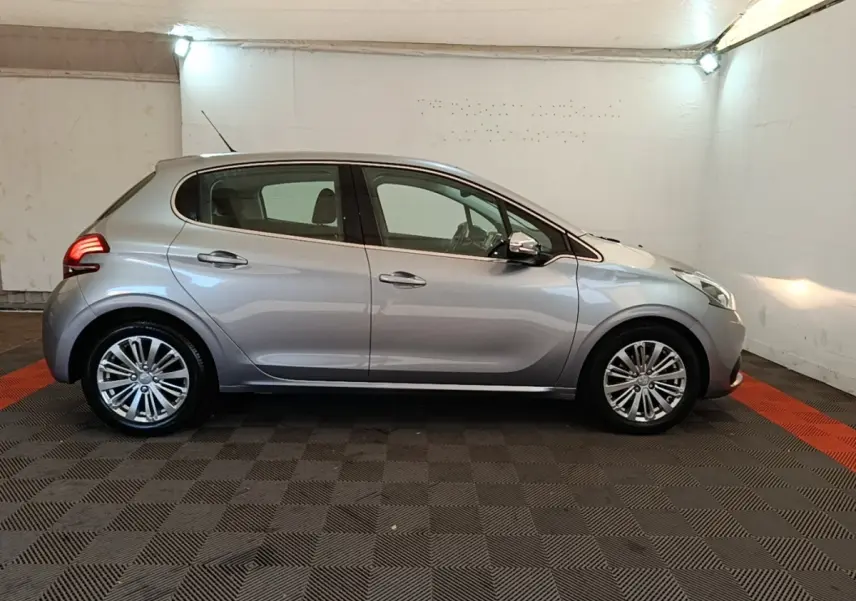 Peugeot 208 Puretech 82 Allure gris clair vue de profil côté gauche dans un garage éclairé.
