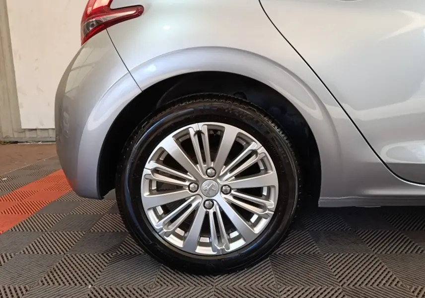 Gros plan sur la roue arrière droite d'une Peugeot 208 gris clair, avec jante alliage et feu arrière partiel visible.