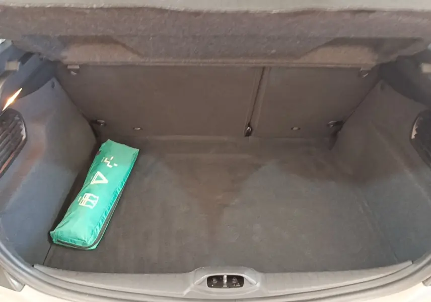 Coffre ouvert de Peugeot 208 gris clair, vue de dessus montrant un kit de sécurité vert à gauche.