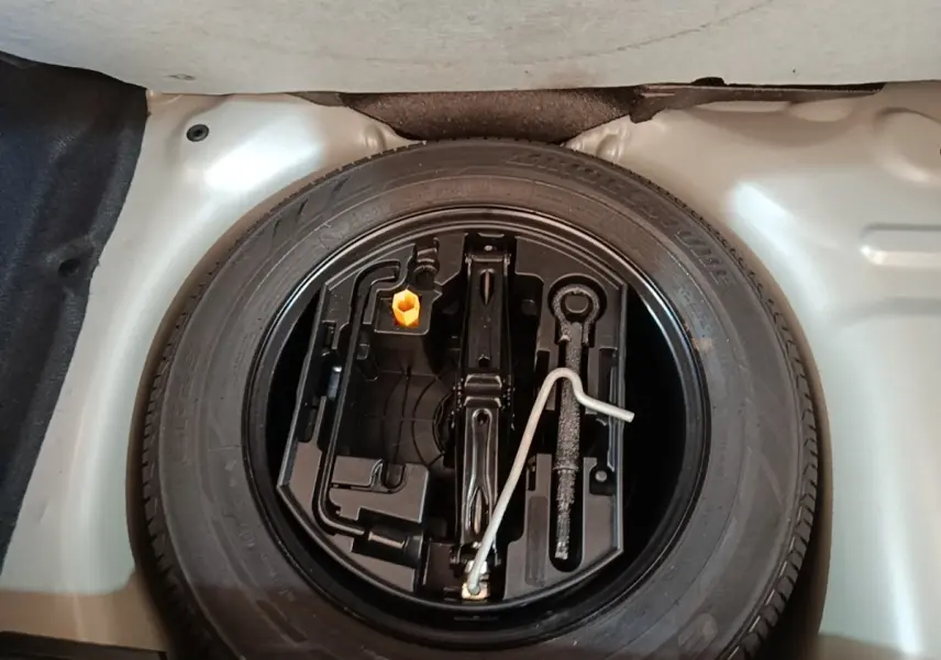 Roue de secours et outillage dans le coffre d'une Peugeot 208 gris clair, vue plongeante sur l'espace rangement.