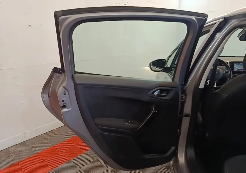 Vue intérieure sur la porte arrière gauche ouverte d'une Peugeot 208 gris clair, avec intérieur noir visible.