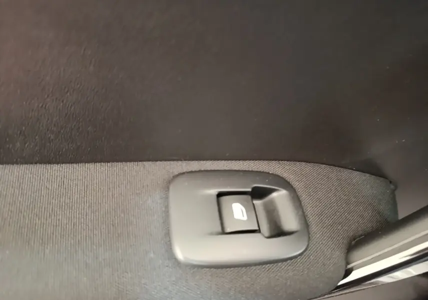 Gros plan sur le bouton de commande de lève-vitre arrière droite d’une Peugeot 208 gris clair Puretech 82 Allure.