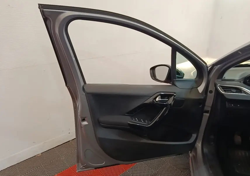 Vue intérieure de la porte avant gauche ouverte d'une Peugeot 208 gris clair, avec garniture noire et commandes électriques.