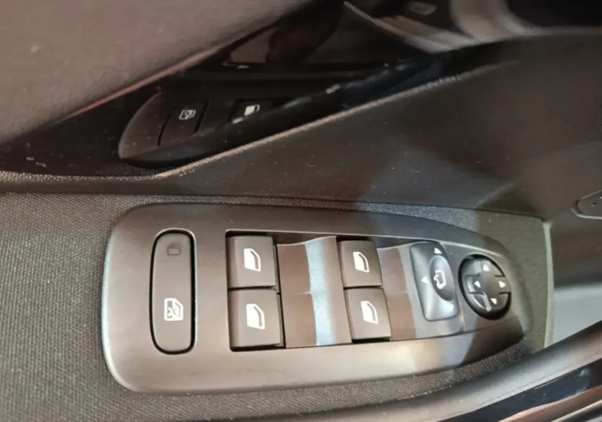 Gros plan sur les commandes de lève-vitres et rétroviseurs côté conducteur d'une Peugeot 208 gris clair.