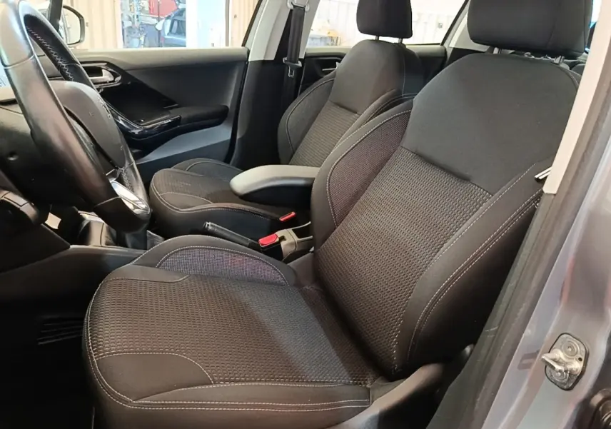 Vue intérieure côté conducteur de la Peugeot 208 gris clair, sièges noirs avec coutures blanches et volant cuir.