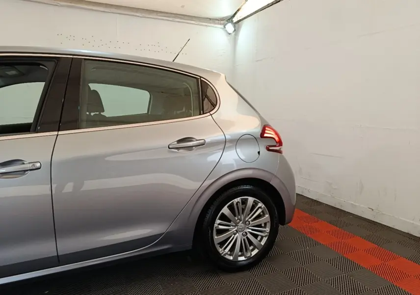 Vue latérale droite sur l'arrière d'une Peugeot 208 gris clair, avec feux arrière allumés dans un garage.