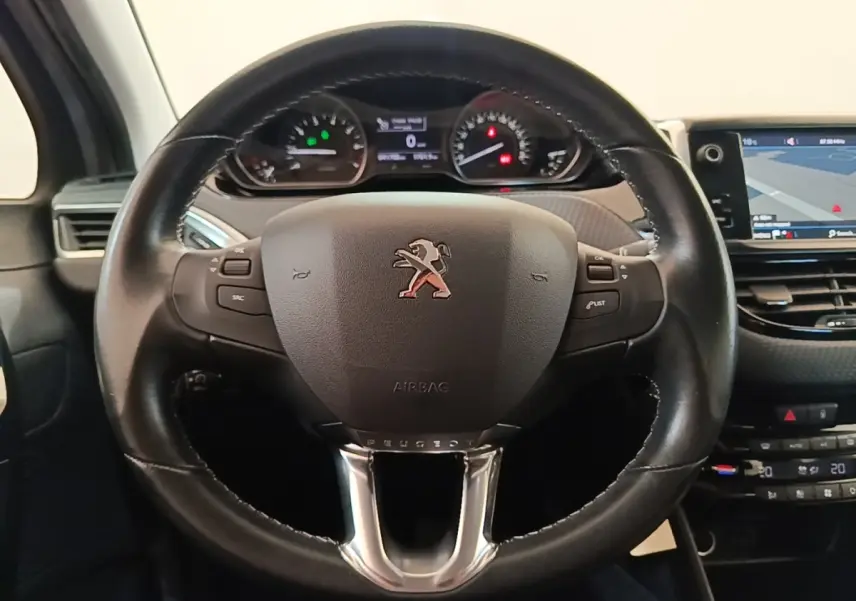 Vue rapprochée du volant cuir noir de la Peugeot 208 Puretech 82 Allure avec tableau de bord et écran tactile visible.