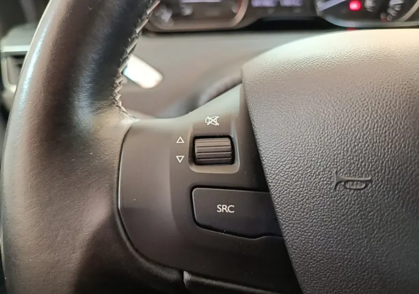 Gros plan sur le volant cuir noir de la Peugeot 208 Puretech 82 Allure, avec commandes audio intégrées.