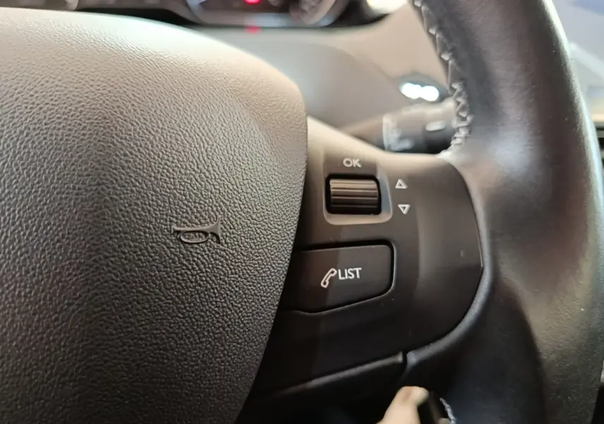 Gros plan sur le volant en cuir noir du Peugeot 208 Puretech 82 Allure avec commandes intégrées côté droit.