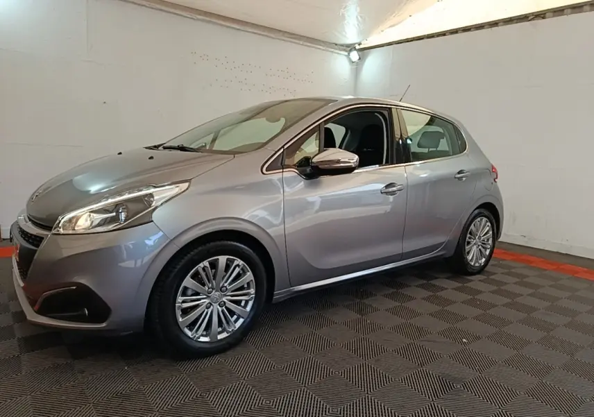 Peugeot 208 gris clair vue 3/4 avant droit en intérieur avec jantes alliage et rétroviseurs chromés.