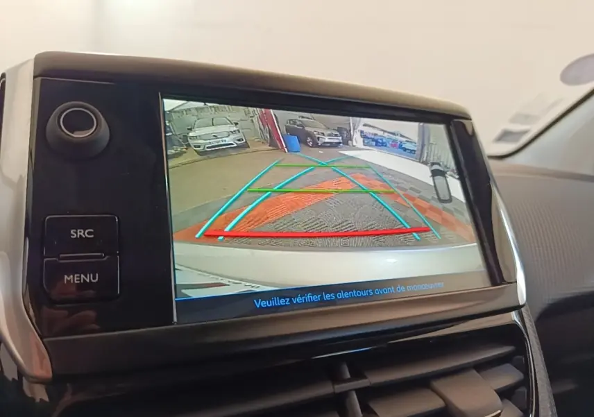 Écran tactile intérieur montrant la caméra de recul d'une Peugeot 208 gris clair, avec lignes de guidage colorées.