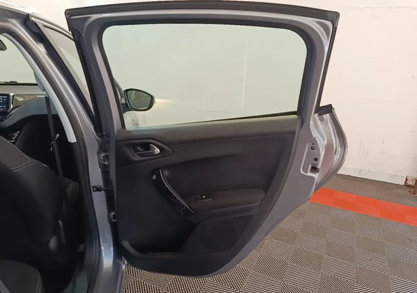 Vue intérieure côté gauche de la porte arrière ouverte d'une Peugeot 208 gris clair, montrant la garniture noire.