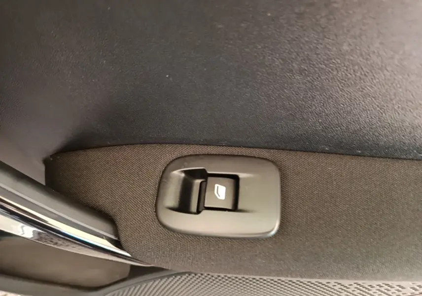 Détail du bouton de commande de lève-vitre sur la porte intérieure tissu d'une Peugeot 208 gris clair.