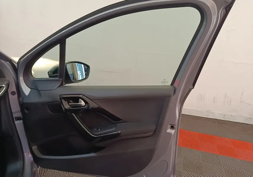 Vue intérieure de la porte avant gauche gris clair d'une Peugeot 208 Puretech 82 Allure avec poignée noire brillante.