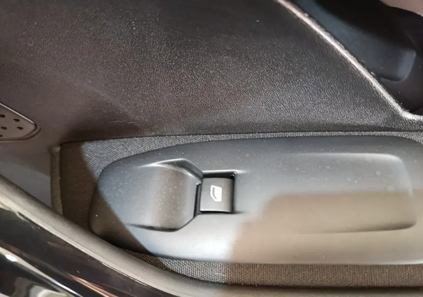Gros plan sur le bouton de commande de lève-vitre côté conducteur dans l'habitacle d'une Peugeot 208 gris clair.