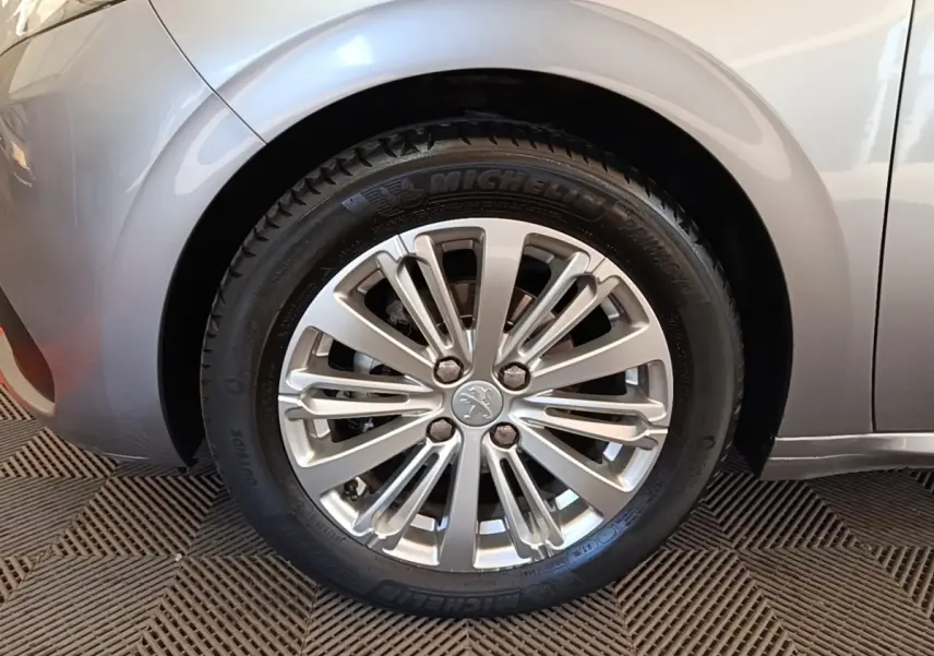 Gros plan sur la roue avant gauche gris clair d'une Peugeot 208 Puretech 82 Allure avec jante alliage.