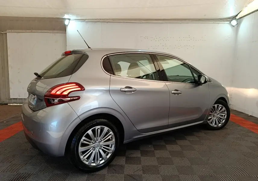 Peugeot 208 Puretech 82 Allure gris clair vue 3/4 arrière droit en intérieur avec feux arrière LED allumés.