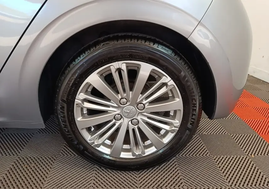 Gros plan sur la roue arrière droite grise claire d'une Peugeot 208 Puretech 82 Allure avec jante alliage multibranches.