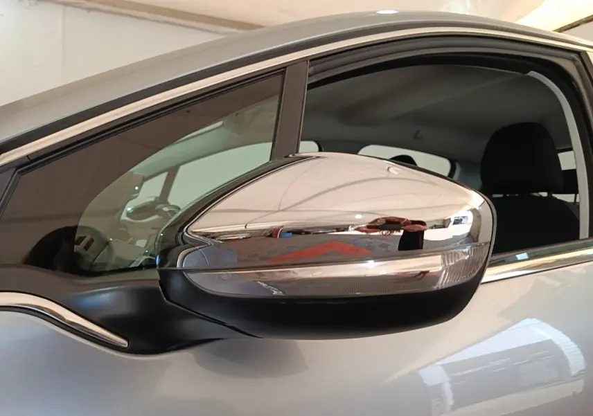 Rétroviseur chromé côté conducteur d’une Peugeot 208 gris clair, vue rapprochée sur la portière avant.