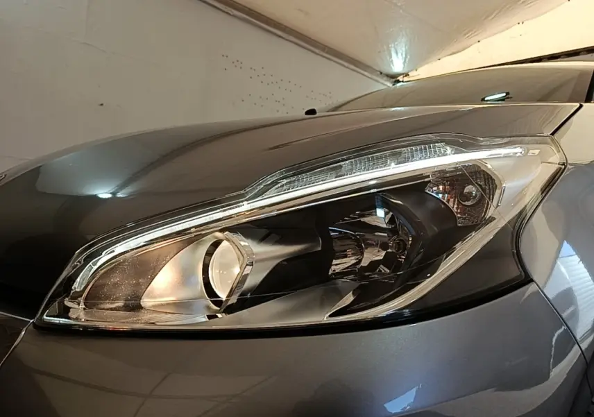 Gros plan sur le phare avant droit de la Peugeot 208 Puretech 82 Allure gris clair, avec reflet lumineux.
