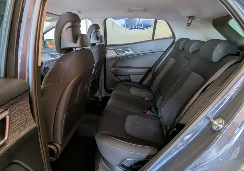 Vue intérieure côté gauche des sièges arrière noirs du KIA SPORTAGE gris eclipse avec porte ouverte et garnitures bois.