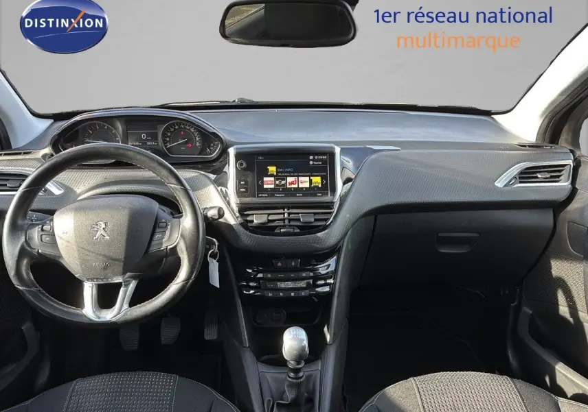 Intérieur noir de la Peugeot 208 2019, vue frontale du tableau de bord avec volant, écran tactile et levier de vitesse manuel.