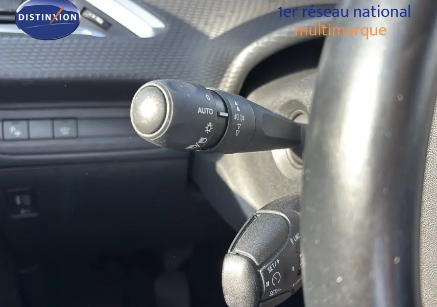 Gros plan sur les commandes au volant d'une Peugeot 208 noire, montrant les leviers de clignotants et régulateur de vitesse.