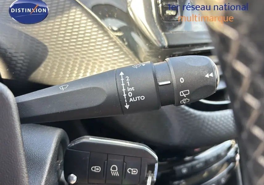 Gros plan sur la commande d'essuie-glace à gauche du volant dans l'habitacle d'une Peugeot 208 noire perle métal.