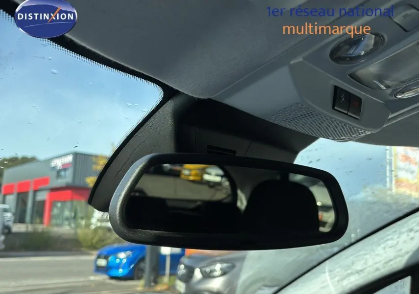 Rétroviseur intérieur d'une Peugeot 208 noire perle métal, avec vue floue sur des voitures en arrière-plan.