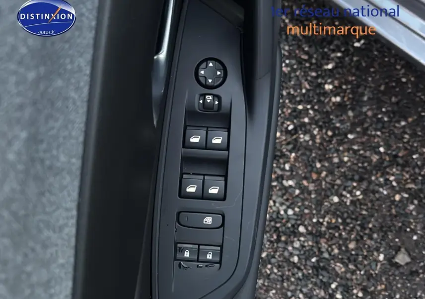 Commande des vitres électriques et des rétroviseurs côté conducteur de la Peugeot 308 gris Artense, porte ouverte sur sol gravillonné.