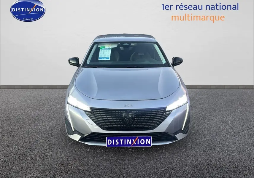 Vue avant d'une Peugeot 308 gris artense 2025 avec phares LED allumés et calandre noire distinctive.