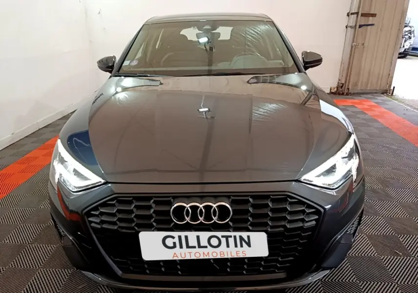 Audi A3 35 TFSI gris foncé vue de face, avec calandre hexagonale noire et phares LED allumés.