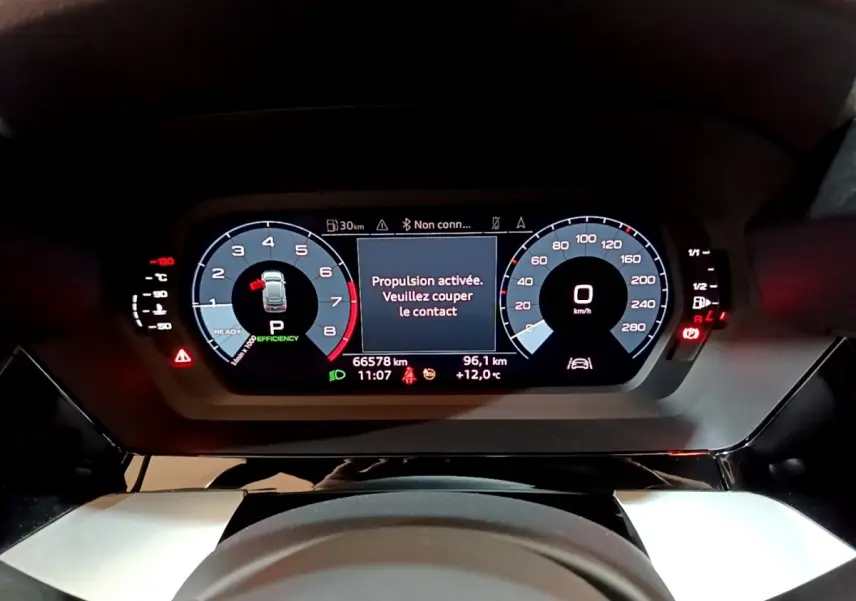 Vue rapprochée du tableau de bord numérique de l'Audi A3 gris foncé, affichant le compteur et les alertes de conduite.