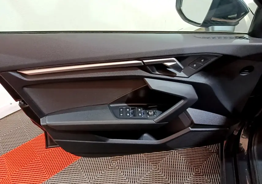 Vue intérieure côté gauche de la porte Audi A3 gris foncé, avec commandes électriques et poignée argentée.