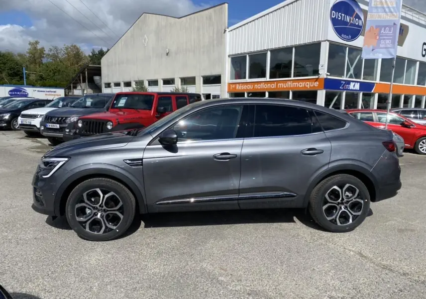 Profil droit d'un Renault Arkana gris foncé 2022 avec vitres surteintées et jantes alliage distinctives, stationné en extérieur.